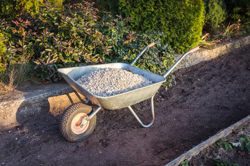 Single wheel garden wheelbarrow loaded with crushed stone prepared for garden path reconstruction in the autumn garden