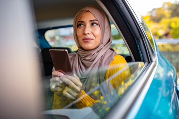 Portrait of happy beautiful young Muslim woman in beige hijab sitting on backseat of car. Beautiful...