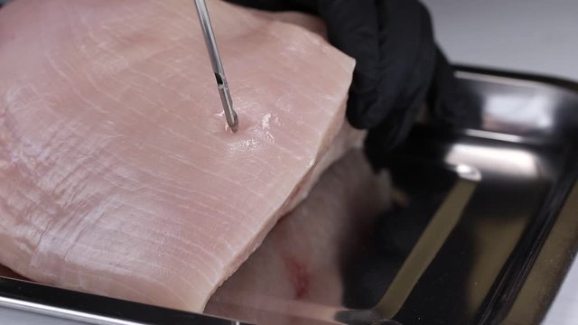 A woman takes a syringe from a metal tray and pumps the solution with nitrite salt into the flesh of a turkey, close-up