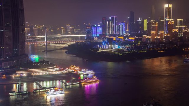 Timelapse coloured Chungking vessels sail along Yangtze and Jialing rivers confluence against Qiansimen Bridge at flashing buildings at night in southwest China