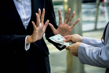 Concept of no bribe stop corruption, businessman or businesswoman holding stack of money in hand offering bribe, hand gesture rejecting the proposal.