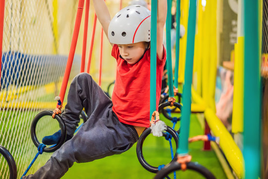 Portrait of 6 years old boy wearing helmet and climbing. Child in abstacle course in adventure playground
