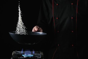 Chef throws rice in a pan. Diet healthy food. Black background for copy text.