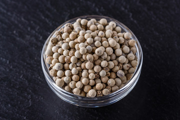 white peppercorns in glass bowl on stone background