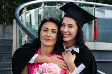 Young beautiful woman graduate hugging her mother at graduation ceremony, University Graduation...