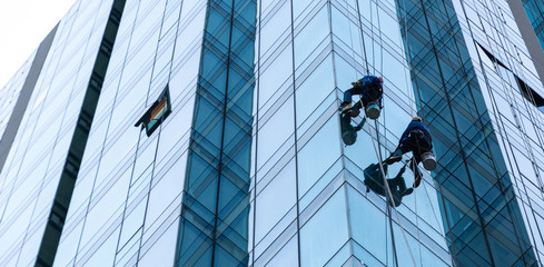 Worker cleaning glass curtain wall at high rise building with rope. Special Job concept.