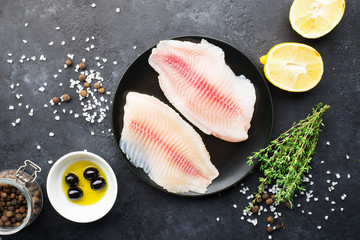 Fototapeta na wymiar Fillet of fish on a kitchen board. Healthy food ingredients. Fresh sea fish fillet, lemons, spices, salt, herbs, spices for a comfortable diet. Against a dark background. Top view.