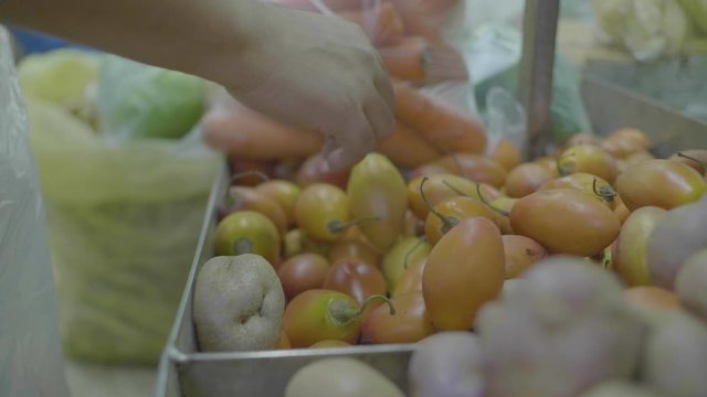 Brown Man's Hand Filling Tamarillo into a Market Bag 