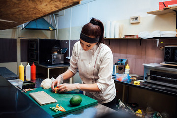 Obraz premium beautiful woman chef prepares fresh sushi in the kitchen of the restaurant