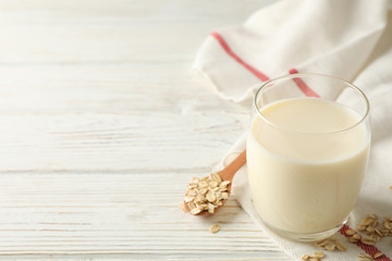 Glass of oat milk, spoon with oatmeal seeds and napkin on white, wooden background, space for text. Closeup