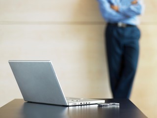 Laptop And Cell Phone On Desk With Businessman In Background