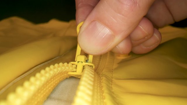 Macro shot of unzipping the zipper of a yellow raincoat.