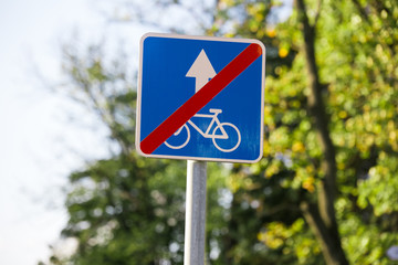 blue red square crossed out road sign End of lane for cyclists close-up on blurred background of sky, trees
