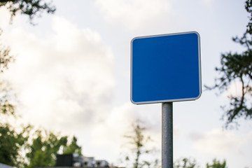blue square blank road sign closeup on blurred background sky with clouds and tree