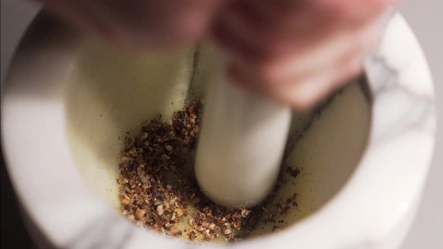 Close up pesting on a mortar some spieces with pepper, ginger and cumin.