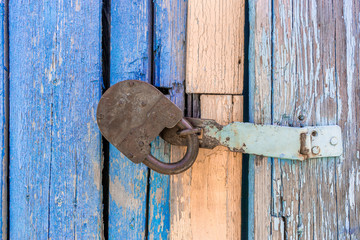 closed iron lock on wooden battered with weathered cracked blue color door of an old country house