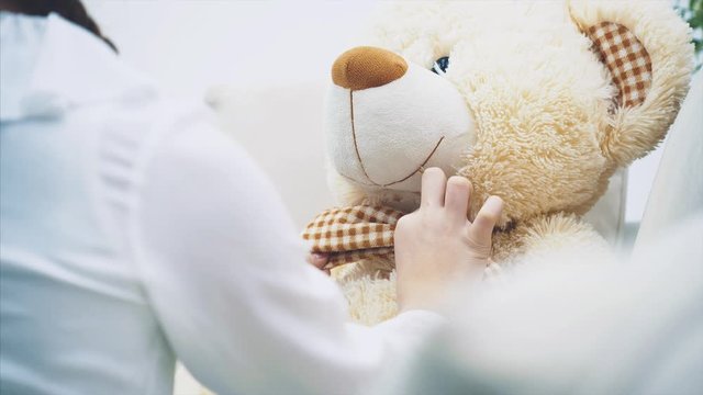 Pretty girl readjusting bow-tie of her teddy-bear and kissing her plush friend. Focus on the bear.