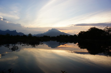 sunset and sunrise are the natural beauty at the end of the night and at dusk giving the perfect color to the sky so the clouds look beautiful to be seen with the beach set against a mountain.