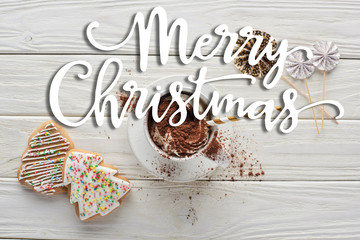 top view of Christmas cookies and cacao in mug with decoration on white wooden table with merry Christmas lettering