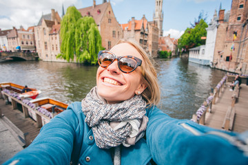 Fototapeta na wymiar Beautiful young girl takes selfie photo on the background of the famous tourist destination with a canal in Bruges, Belgium