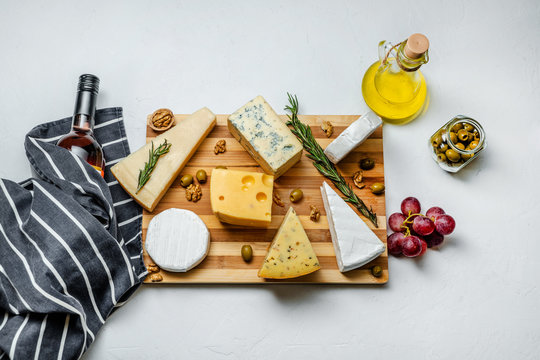 Different Sorts Of Cheese. Cheese Platter With Different Cheese, Bottle Of Wine, Nuts And Spices On White Background