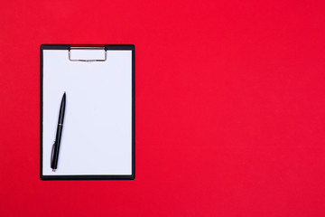 Clipboard with white sheet and pen on a red background. View from above. space for text