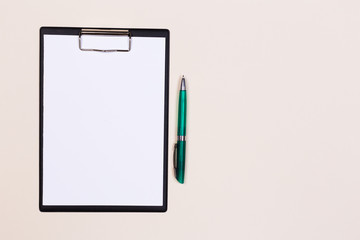 Clipboard with a white sheet and pen on a light background. View from above. space for text