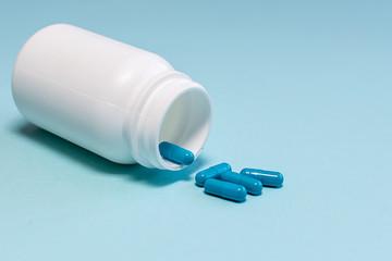 Blue medical pills or capsules in white plastic bottle on blue pastel background. Template medical blog social media.