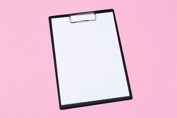 Clipboard with white sheet and pen on a pastel pink background. View from above. space for text