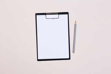 Clipboard with a white sheet and pen on a light background. View from above. space for text