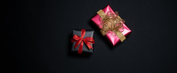 Top view of black gift box with red and black ribbons isolated on black background.
