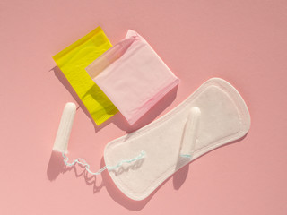 Flat lay menstrual tampons and pads on a pink background with hrad light. Menstruation cycle concept