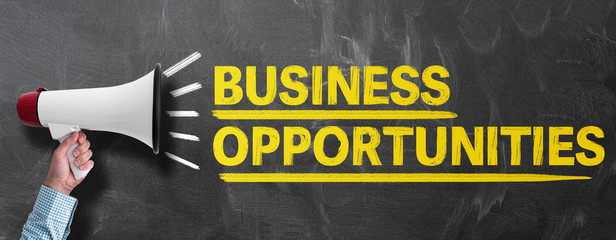 hand holding megaphone or bullhorn against blackboard with text BUSINESS OPPORTUNITIES