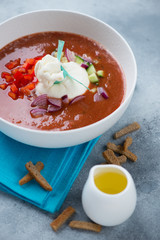 White bowl of gazpacho soup with burrata cheese, vertical shot over light-blue stone background