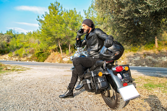 Young man with mobile phone on motorcycle in nature. Motorcycle driver talking on the phone.