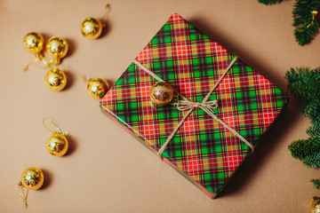 Christmas composition. Christmas gift, fir branches on carton background. Flat lay, top view, copy space. Plaided gift with christmas ornaments around.