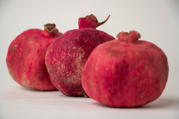 three red pomegranates with a dry rough skin on a light background
