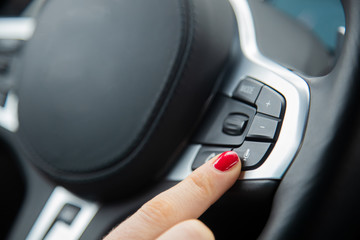 the finger of a female hand points to the microphone button on the steering wheel, the equipment of a modern car. close-up, soft focus, blur background
