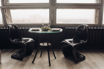 Close-up of round table served for two for Christms dinner. Silver candle decorated with natural fir branches, two flutes, pairs of plates with decorative handmade Christmas trees.