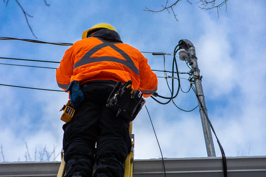 A low angle shot of a domestic service provider engineer installing new fiber optic cables to a residential home, working from ladders with tool belt