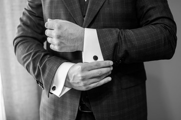 A groom fastening a cuff-link on the shirt black and white