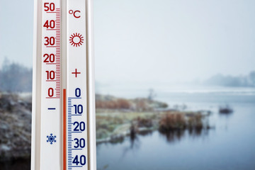 The thermometer on the background of the spring landscape with the river shows 5 degrees above zero_