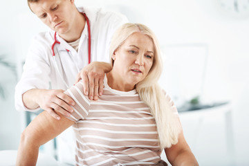 Fototapeta premium Doctor examining mature woman with joint pain in clinic