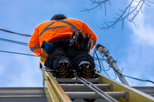 A professional telecoms installer is seen from directly below, installing fiber cables from the top of a ladder on the roof of a residential property