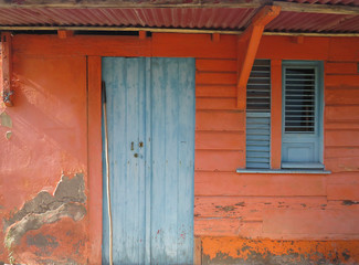 Rusted blue front door and window over orange facade. Tropical construction. Martinique, Antilles. French West Indies