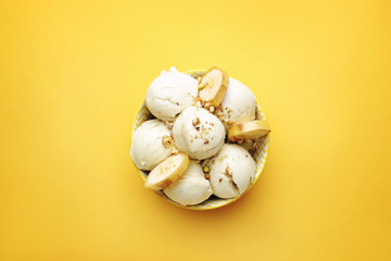 Bowl with tasty ice-cream, nuts and banana on color background