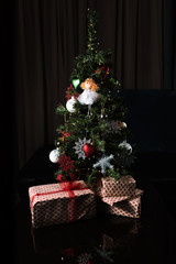Beautiful small decorated Christmas Tree and many gifts at home with a darkened background