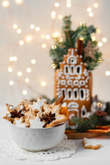 Delicious homemade baked gingerbread cookies in white bowl and house with white icing. Rustic style, candles and christmas lights. Cozy home atmosphere, festive mood, holiday inspiration