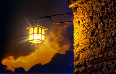 Illuminated street lamp fixed to a brick wall with a fairytale night sky