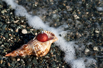 Christmas ball, seashell and pebbles at the beach